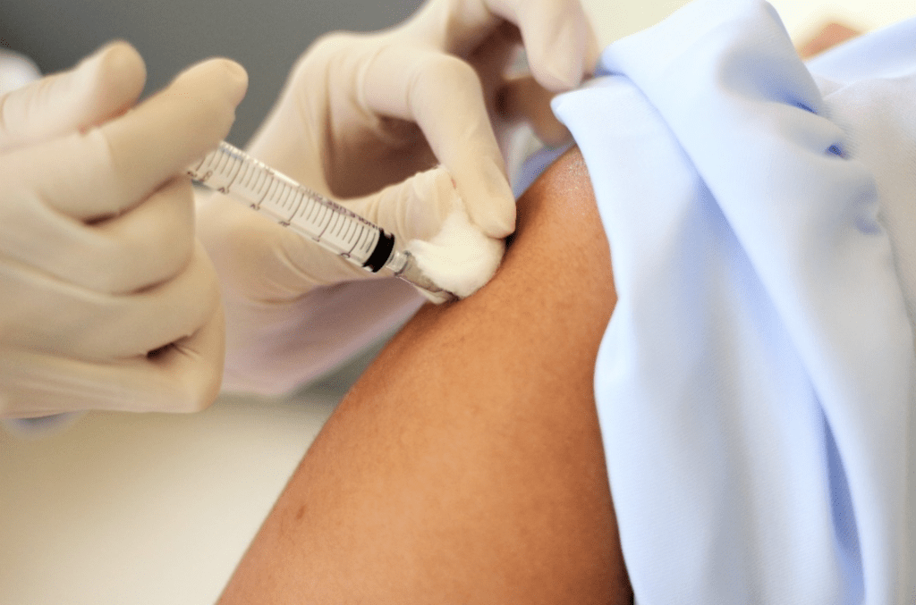 Hand with rubber gloves injecting shot into an arm