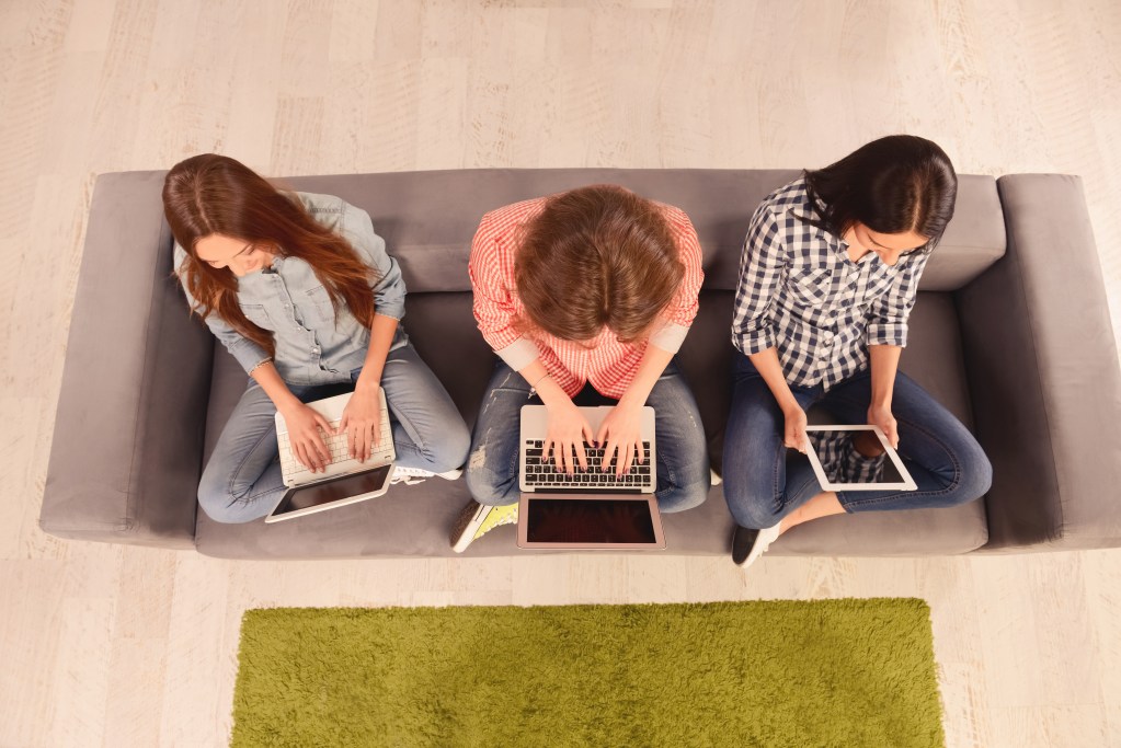 Top view of three tweens sitting on a couch, working on laptops and a tablet