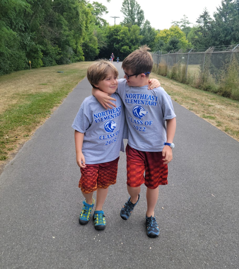 Brothers in matching outfits walking, arms around each other, smiling and looking at each other.