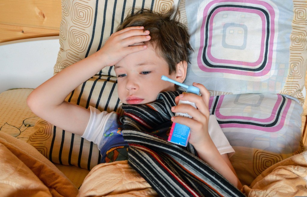Boy wearing scarf holding his head while holding medicine with other hand