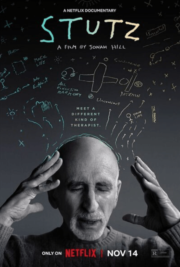 Black and white promotional picture from the documentary film Stutz with Dr. Phil Stutz, center, eyes closed, hands next to his head as if he's thinking, images of his drawings are behind his head. Text reads: A Netflix Documentary Stutz, A Film By Jonah Hill. Only on Netflix, Nov 14.
Imbedded in photo is link to trailer of the film.

